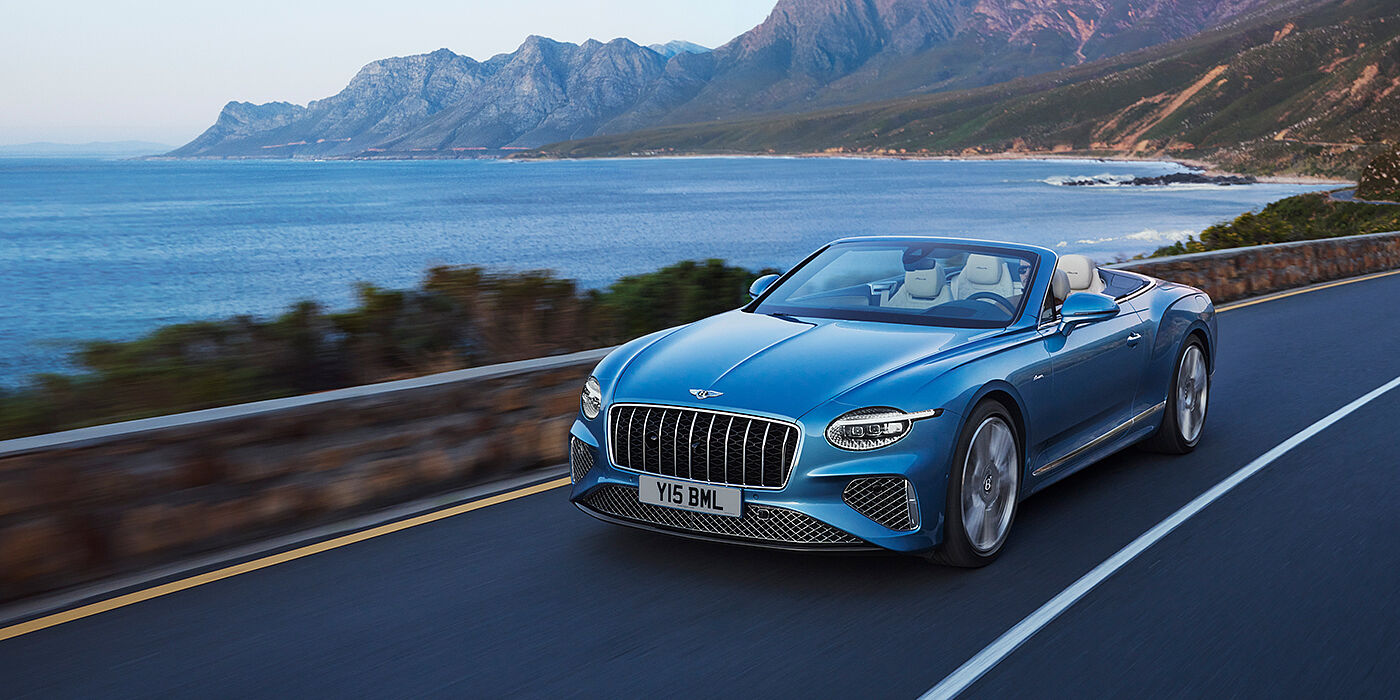 Bentley Bahrain New Bentley Continental GTC Azure convertible in Light Windsor blue paint with 22 inch Azure wheels and chrome grill, driving dynamically by the sea