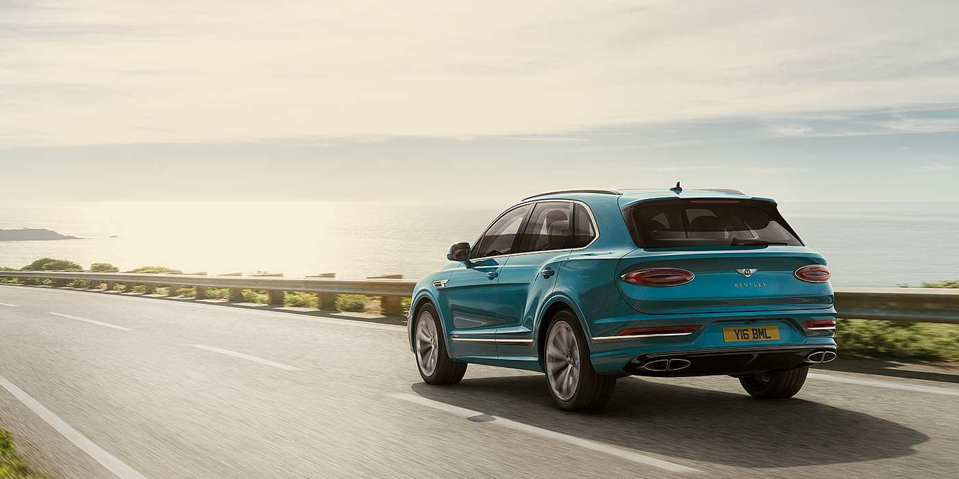 Bentley Bahrain Bentley Bentayga Azure luxury SUV rear three quarter in Topaz Blue by Mulliner paint, driving on an ocean road.