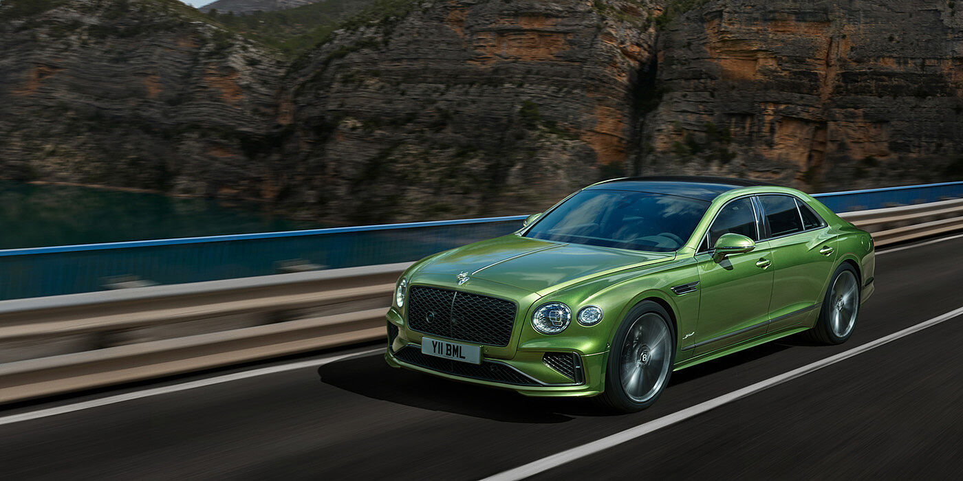 Bentley Bahrain Bentley New Flying Spur Speed v8 hybrid sedan driving dynamically on a mountain road in Tourmaline Green paint