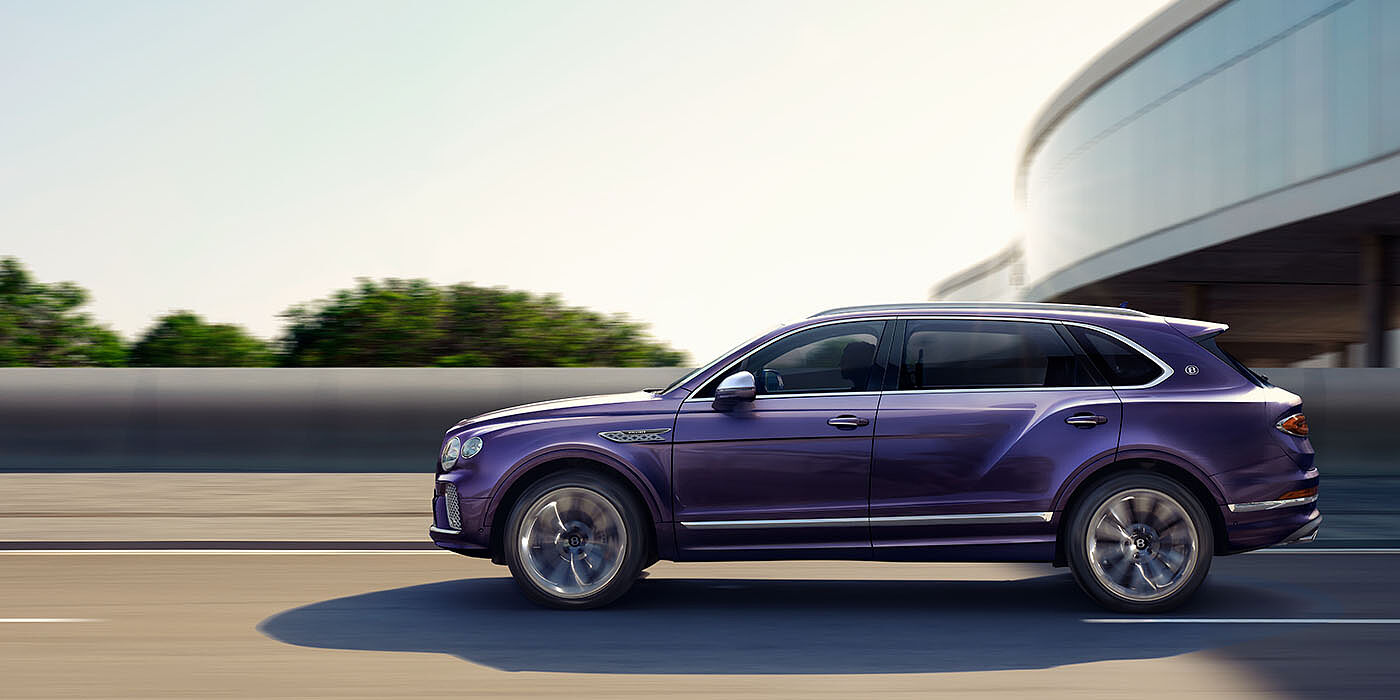 Bentley Bahrain Bentley Bentayga Extended Wheelbase Mulliner luxury SUV profile in Tanzanite Purple paint, driving on an country road past trees.