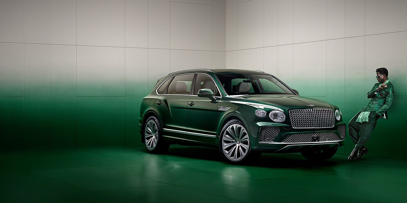 Bentley Bahrain Wisdom K leans against wall next to Bentley Bentayga Extended Wheelbase Atelier Edition SUV in Light Emerald green paint