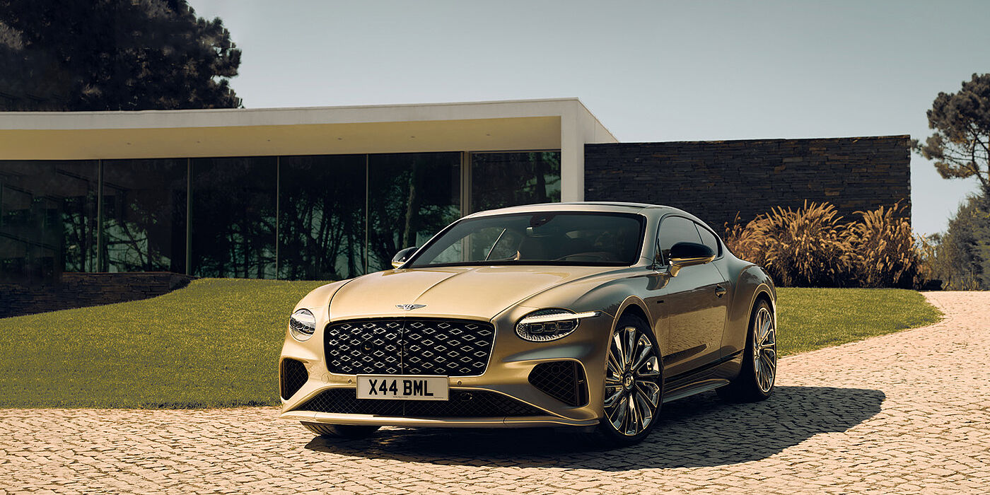 Bentley Bahrain Bentley Continental GT Mulliner coupe front three quarters in Patina paint parked outside a glass fronted building with a grass lawn behind it