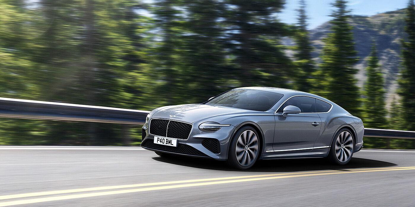 Bentley Bahrain New Bentley Continental GT coupe in Silverlake paint and 22 inch ten-spoke wheels, driving dynamically on a tree-lined road in the sunshine