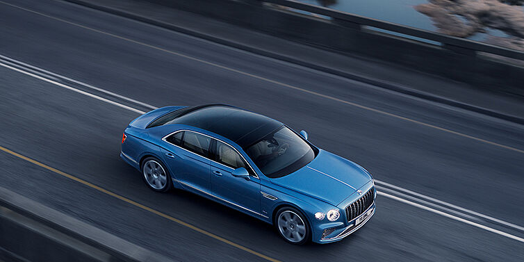 Bentley Bahrain New Bentley Flying Spur Azure sedan in Light windsor blue paint by Mulliner, with 22 inch Azure wheels seen from overhead driving dynamically on a country road