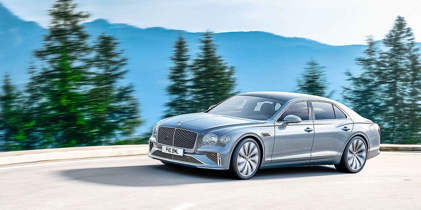 Bentley Bahrain New Bentley Flying Spur sedan side view in Silverlake paint with ten spoke wheels and chrome matrix grille driving dynamically on a mountain road