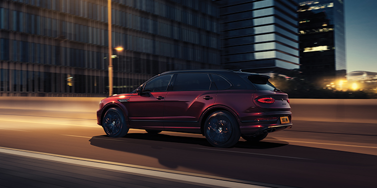 Bentley Bahrain Bentley Bentayga Extended Wheelbase Mulliner SUV in Cricket Ball red paint driving dynamically in city at night